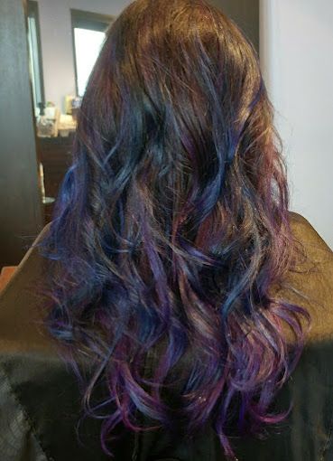 A woman with purple and blue hair is sitting in a chair.