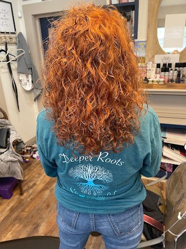 A woman with red curly hair is wearing a t-shirt that says `` deeper roots ''.