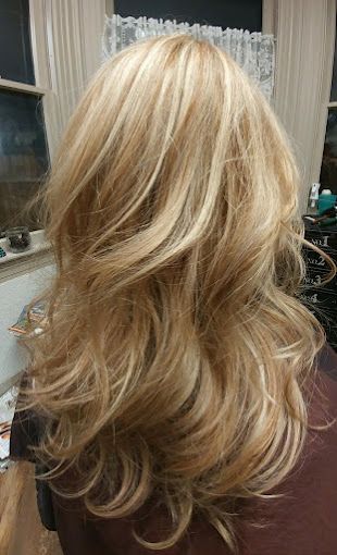 A woman with long blonde hair is sitting in a chair in front of a window.