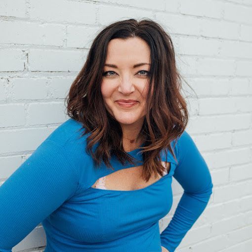 A woman in a blue shirt is standing in front of a white brick wall.