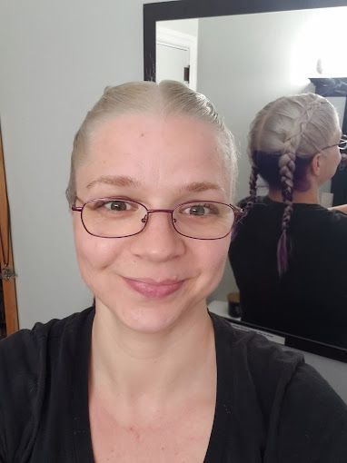 A woman wearing glasses is taking a selfie in front of a mirror.