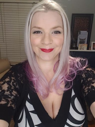 A woman with pink hair is taking a selfie in a black and white dress.