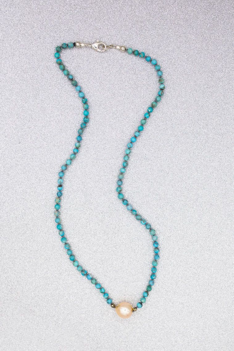 A necklace with turquoise beads and a pearl on a white surface.