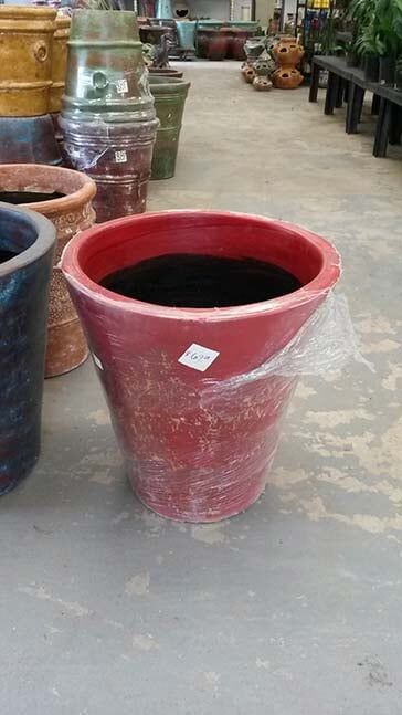 A red pot is sitting on a concrete floor next to other pots.