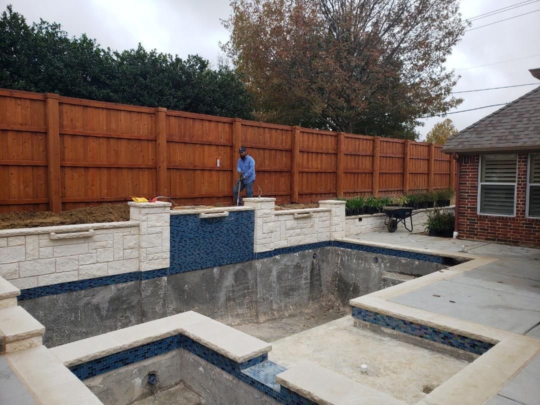 A man is standing next to an empty swimming pool in front of a wooden fence.