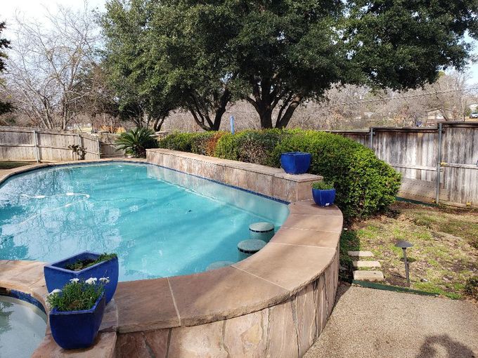 A large swimming pool in a backyard with blue potted plants.