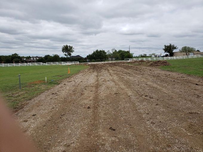 A dirt road going through a grassy field on a cloudy day.