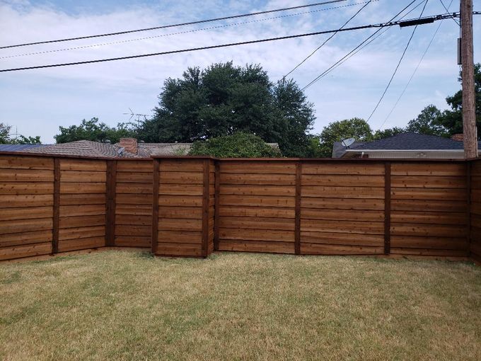 A wooden fence surrounds a lush green lawn in a backyard.