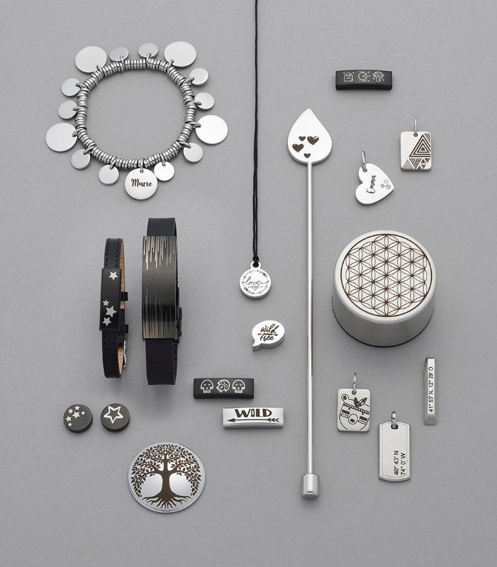 Sieraden: zilveren armbanden, hangers en broches, gerangschikt op een grijze ondergrond. ENERGETIX graveerservice