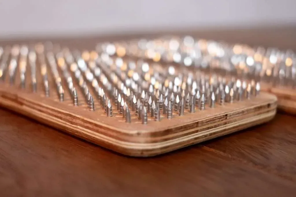 Houten plank met rijen scherpe metalen spijkers, waarschijnlijk een sadhu-plank voor voetmassage.