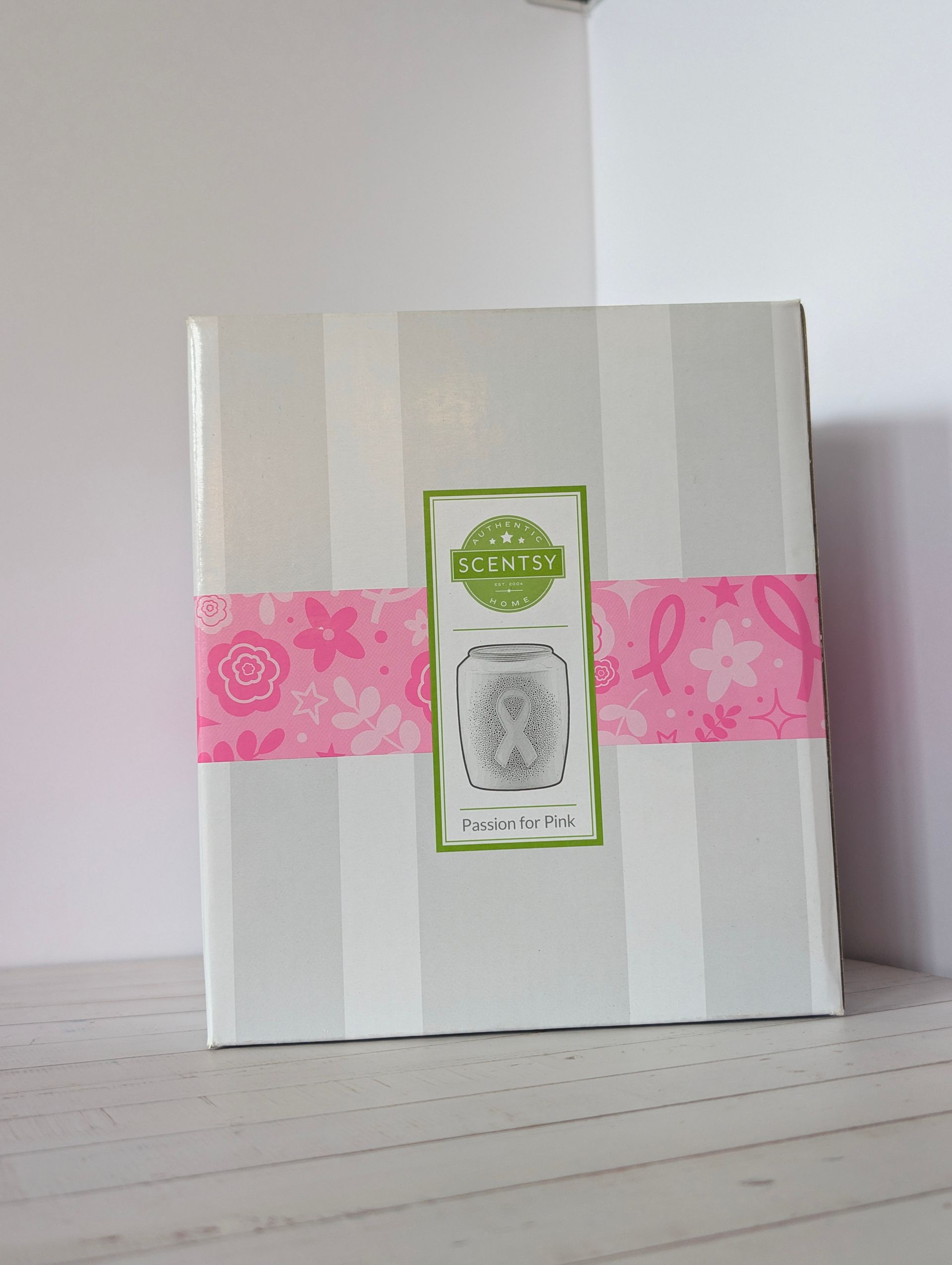 Witte doos met grijze strepen, roze lint en groen etiket, op een witte ondergrond. Scentsy Passion for Pink
