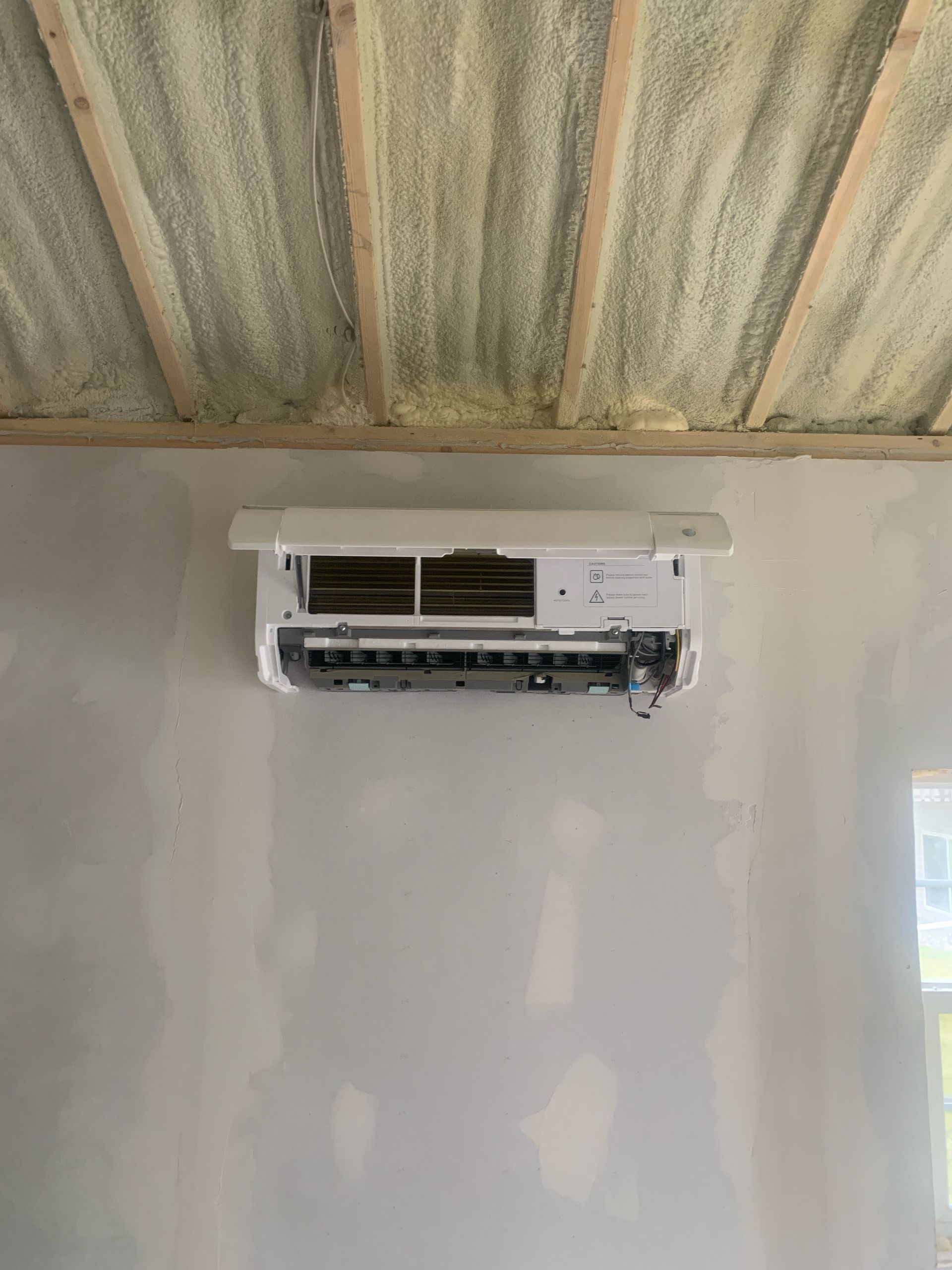 HVAC technician in white hard hat, inspecting air conditioning unit with yellow multimeter outside.