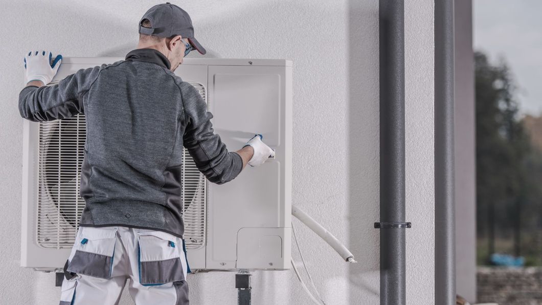 Man in work clothes installing a unit on a building's exterior wall.