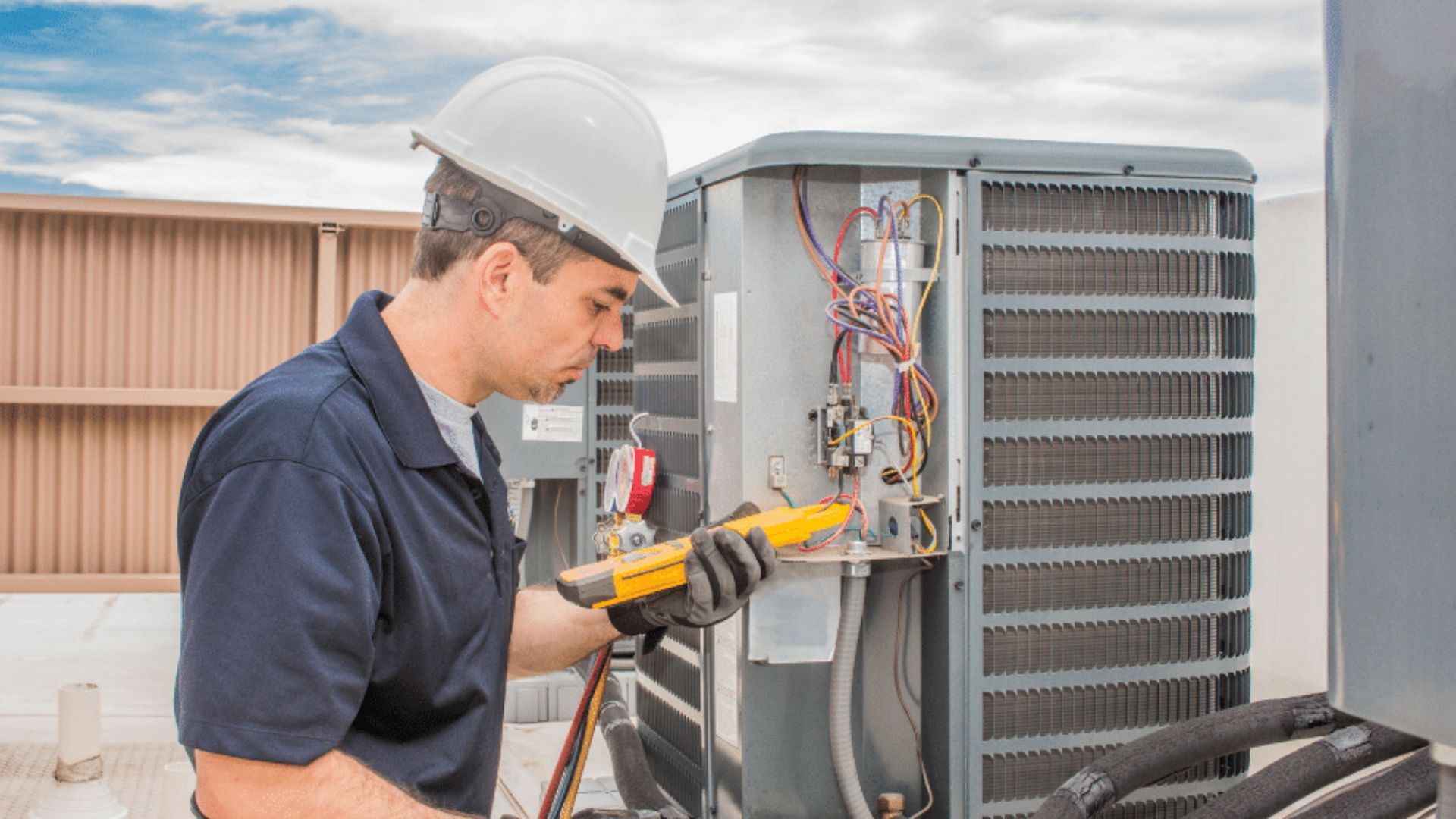 HVAC technician in white hard hat, inspecting air conditioning unit with yellow multimeter outside.