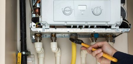 Person using pliers on gas line connected to a boiler.