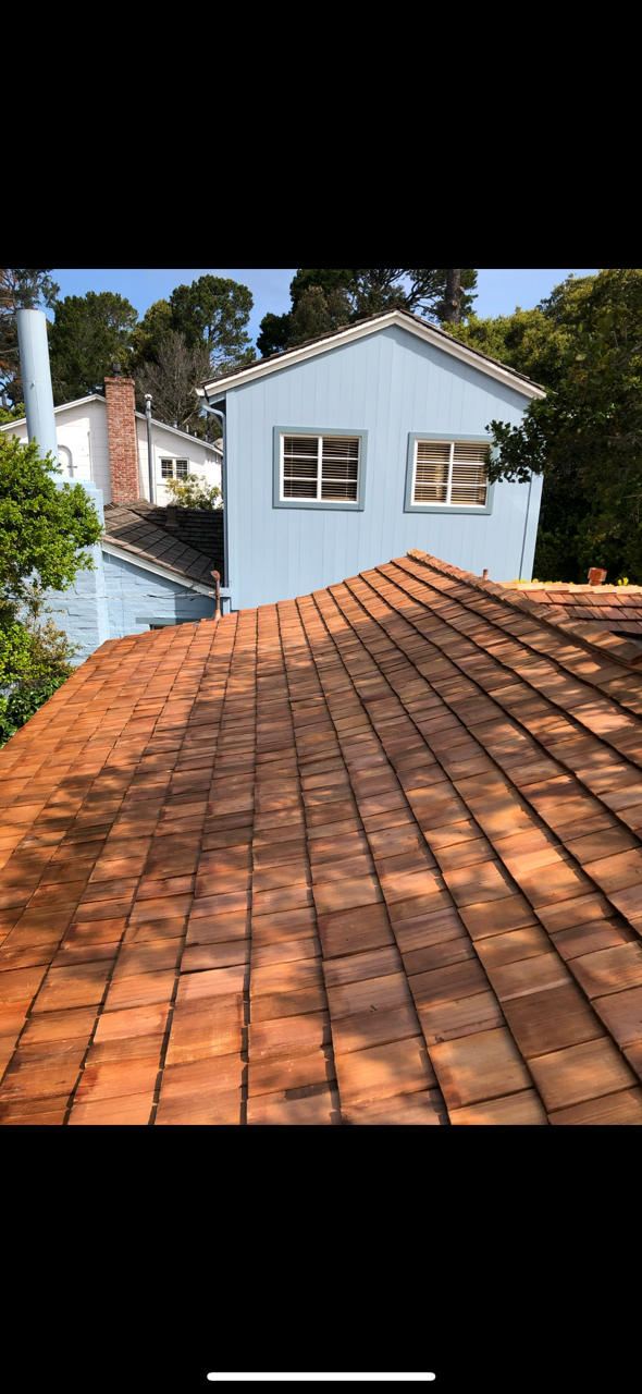 Roofer using a nail gun to install asphalt shingles on a roof.
