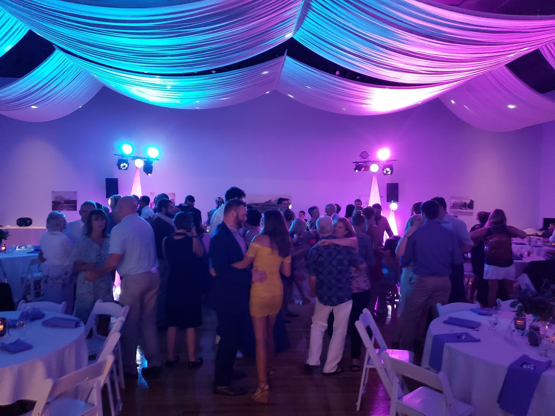 A large group of people are dancing in a room with purple lights.