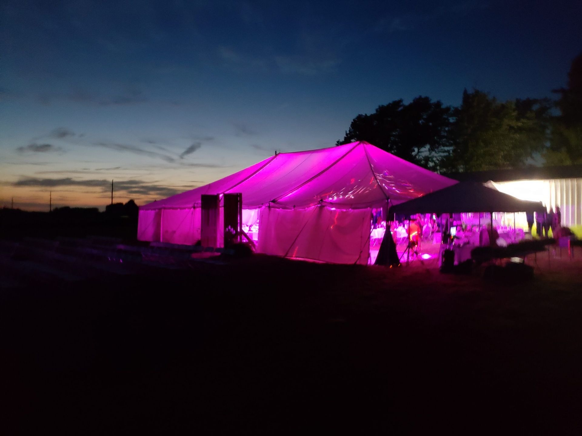 A large tent is lit up with pink lights at night.