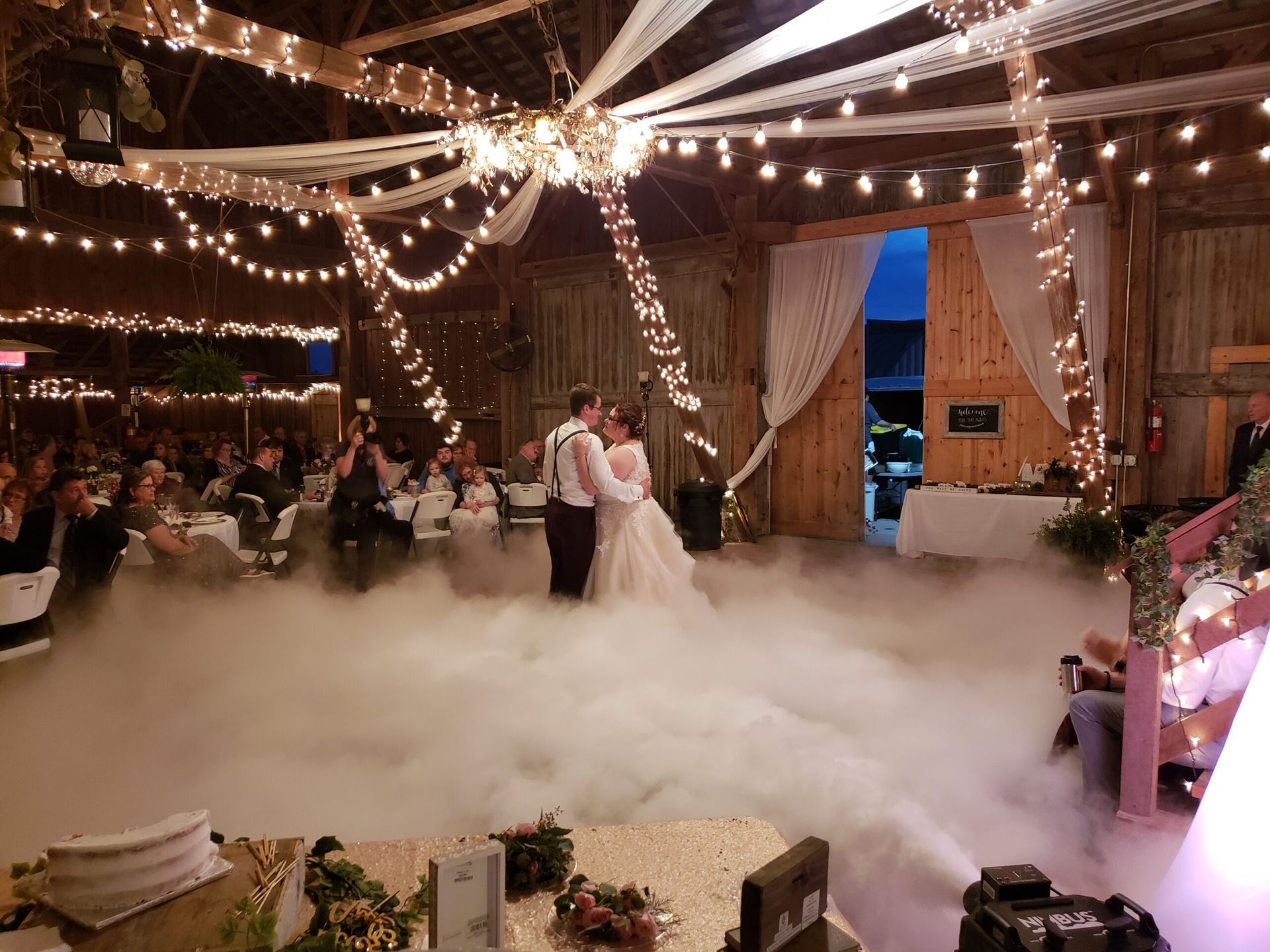 A bride and groom are dancing in a barn with smoke coming out of the ceiling.