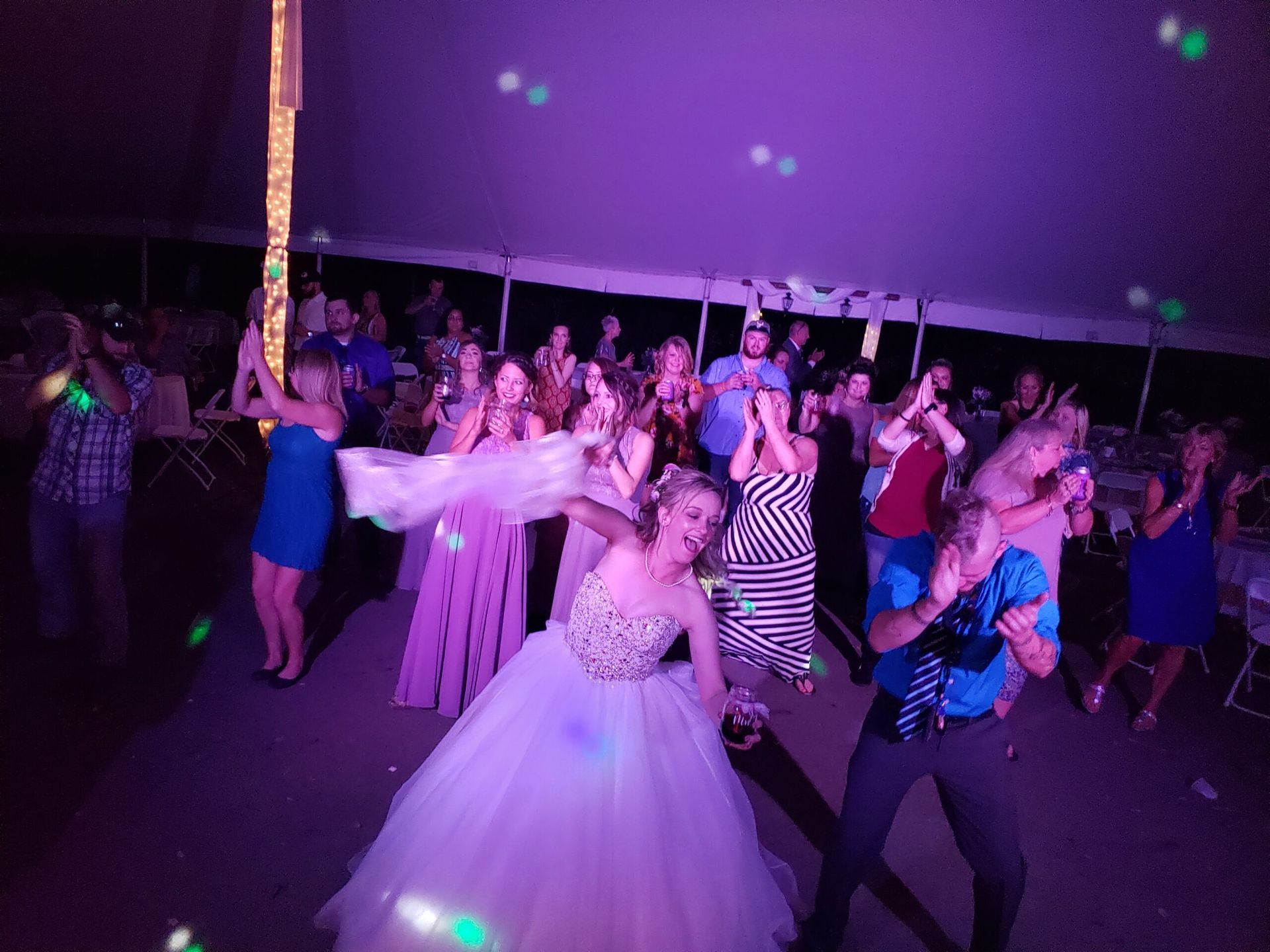 A bride and groom are dancing at a wedding reception under a tent.