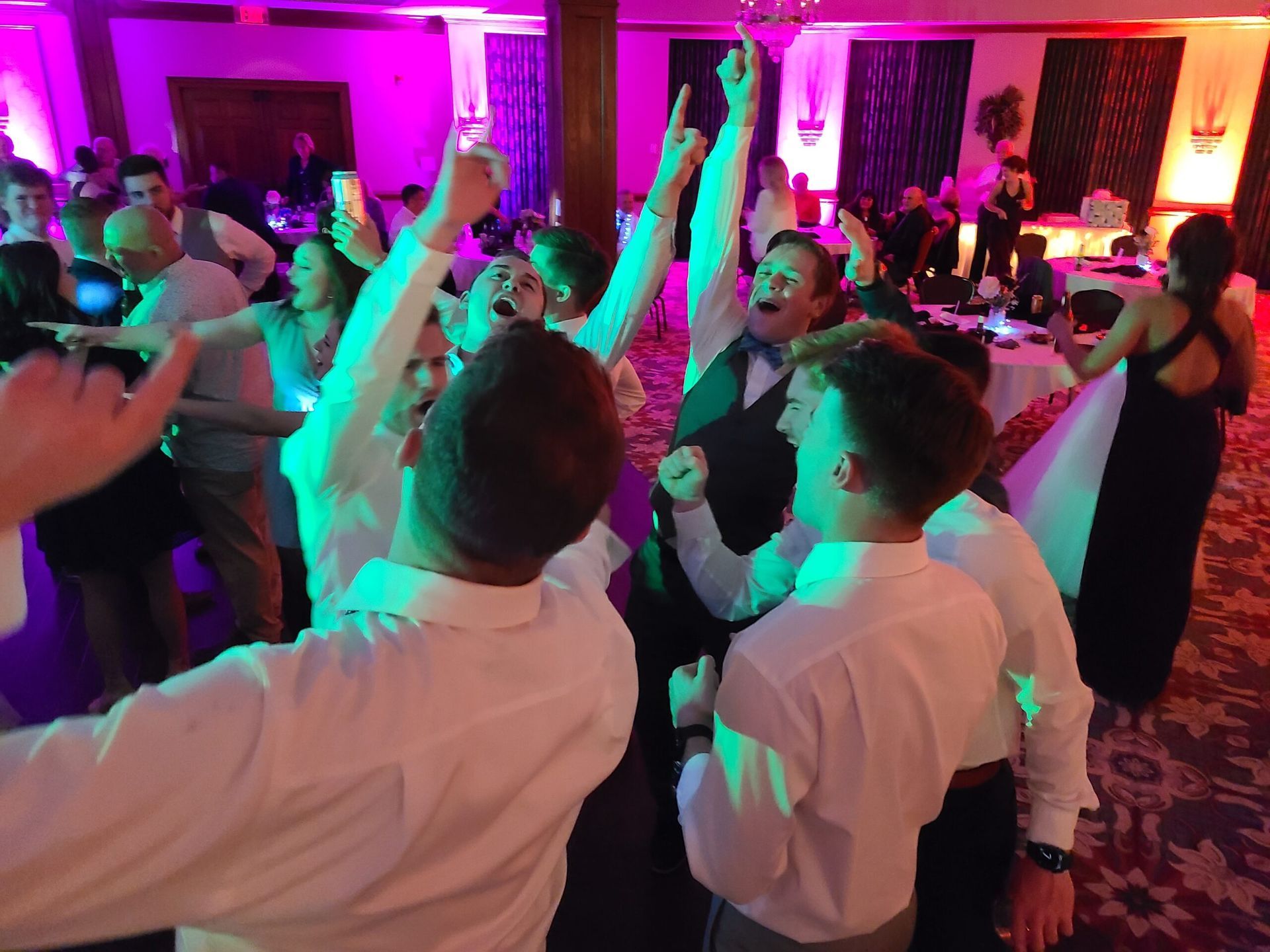 A group of people are dancing in a room with purple lights.