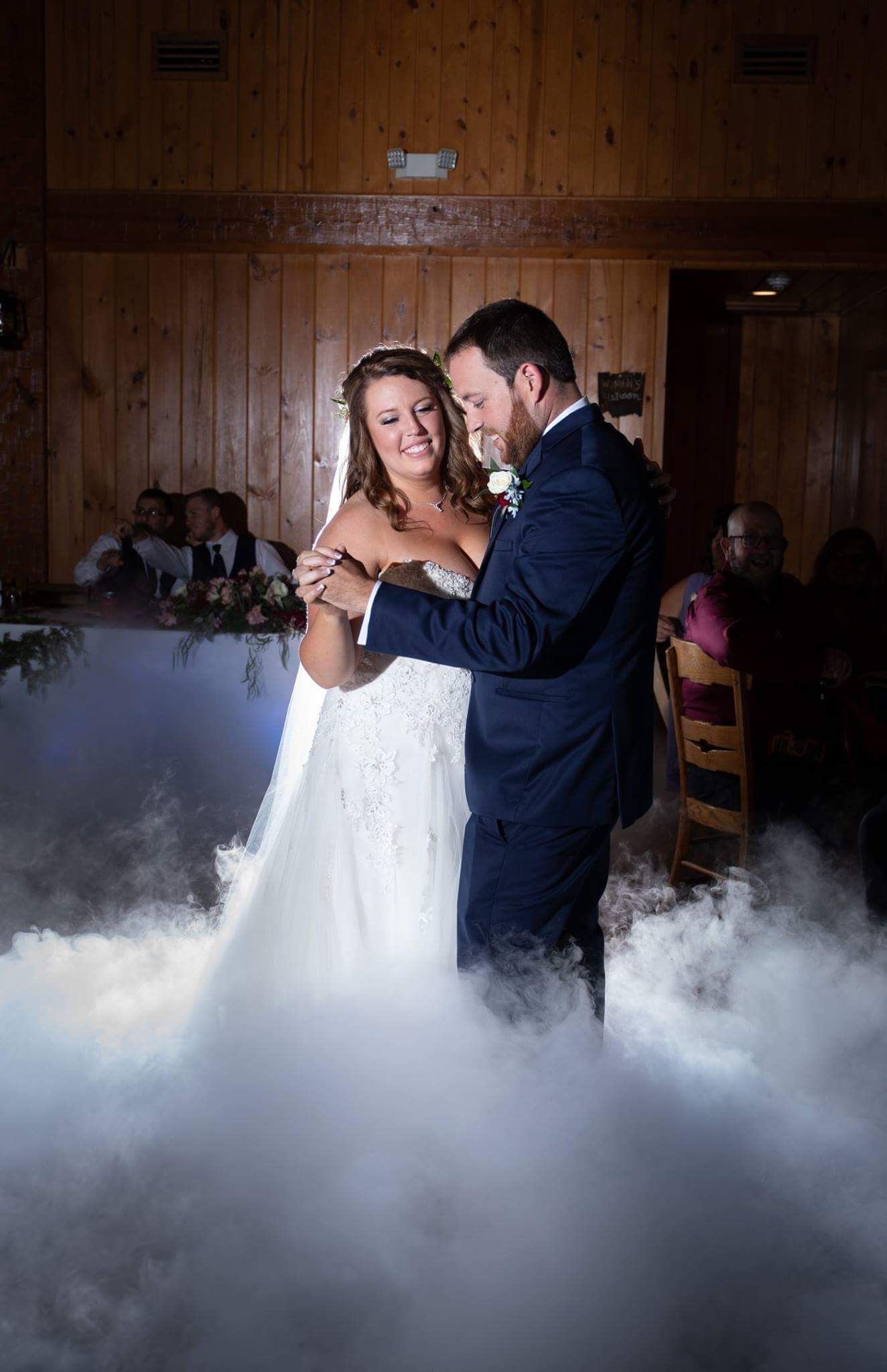 A bride and groom are dancing in the fog at their wedding reception.