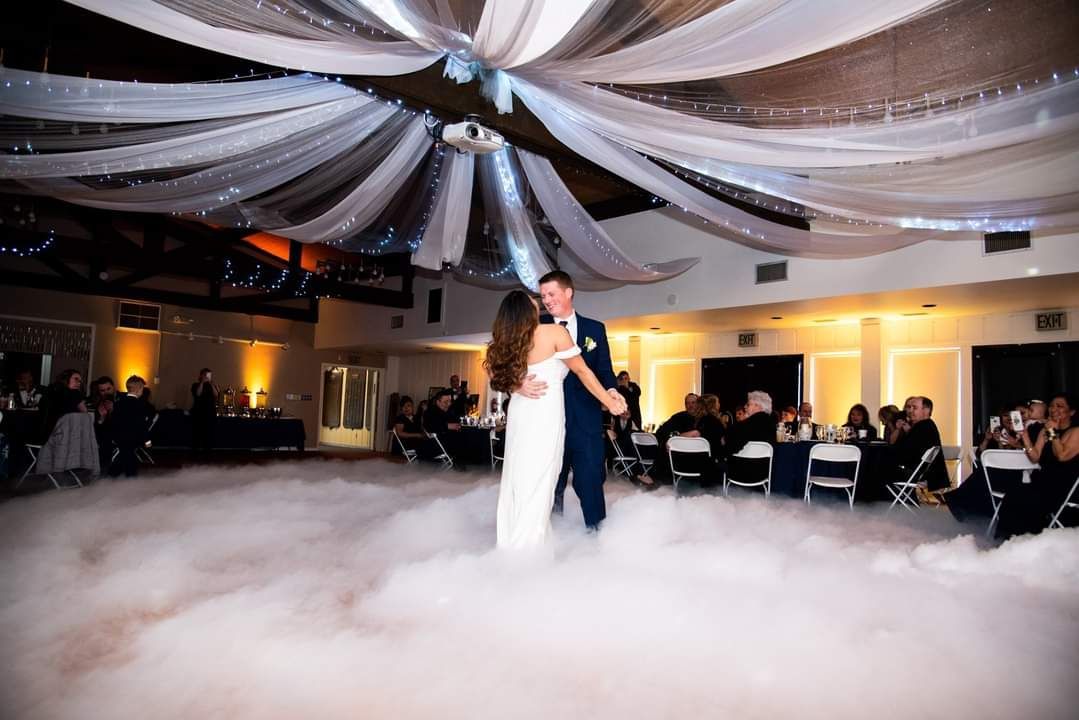 A bride and groom are dancing in the fog at their wedding reception.