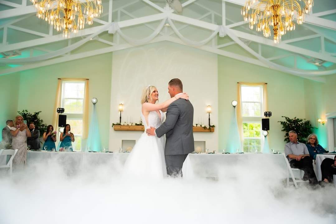 A bride and groom are dancing in a room with smoke coming out of the ceiling.
