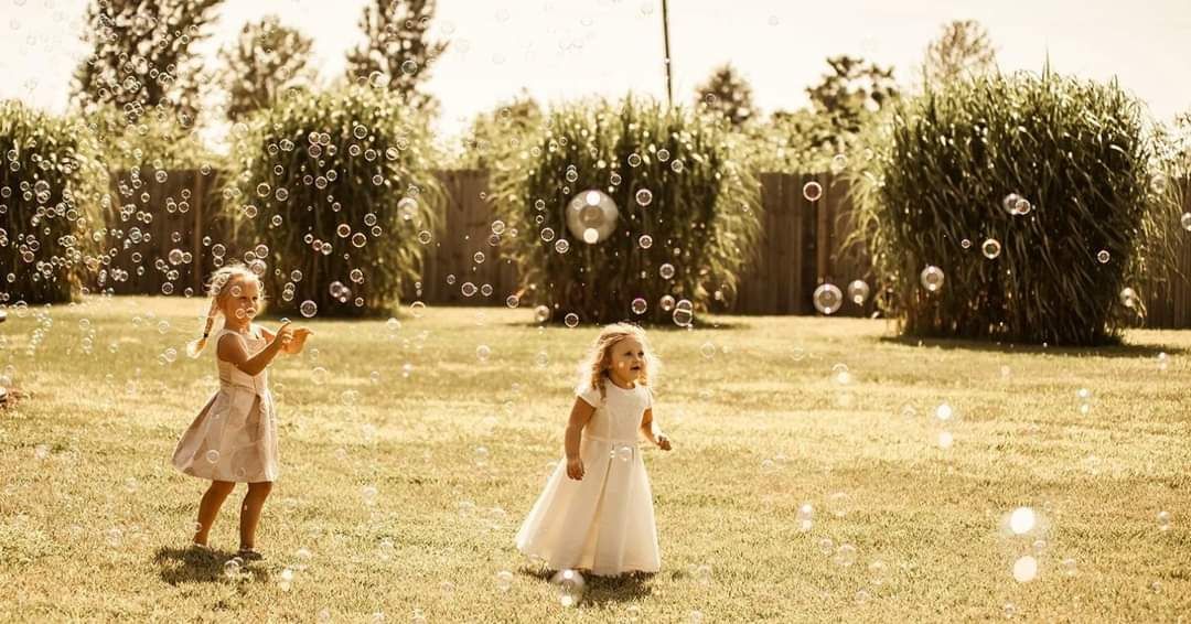 Two little girls are blowing soap bubbles in a park.