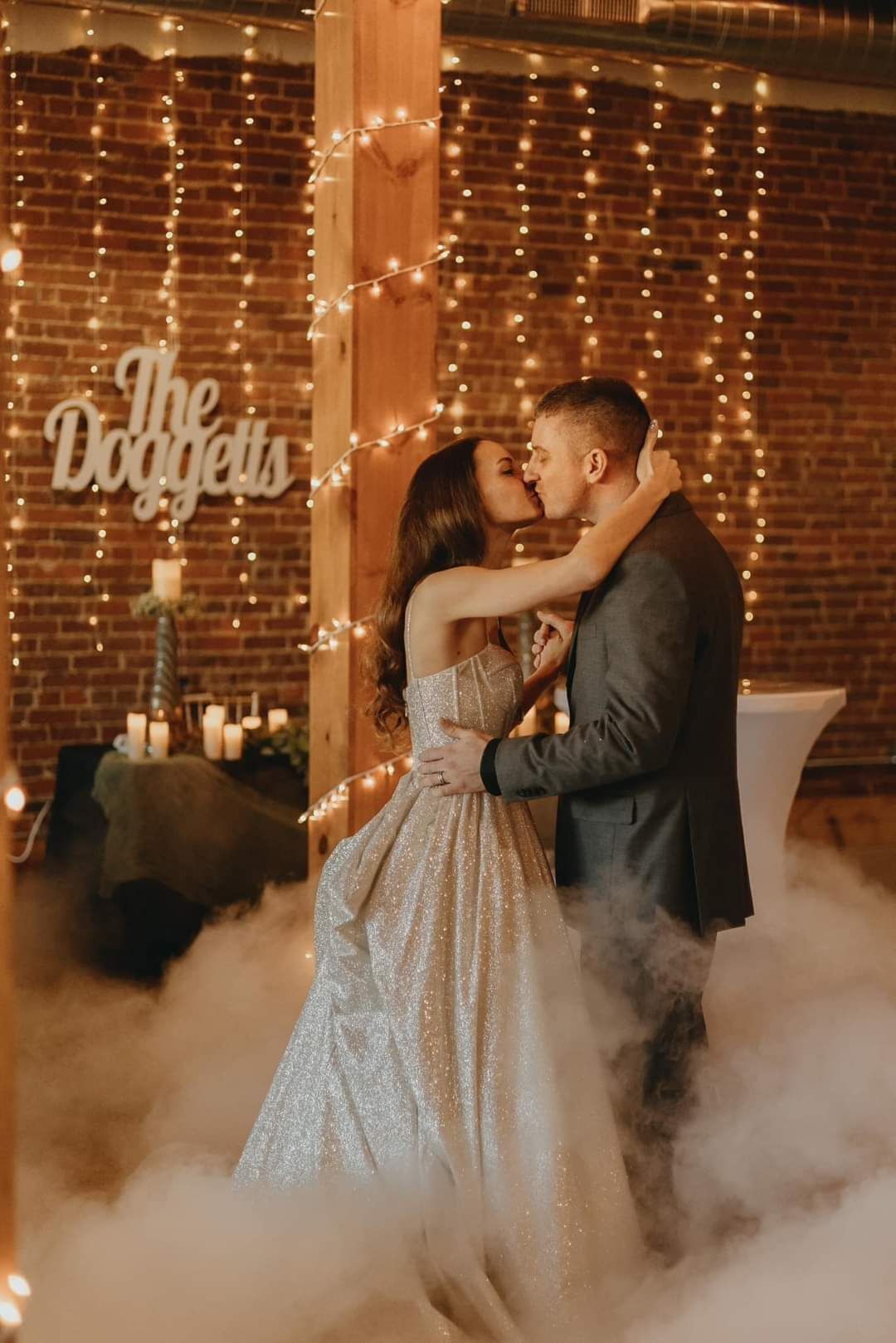 A bride and groom are kissing in front of a brick wall.