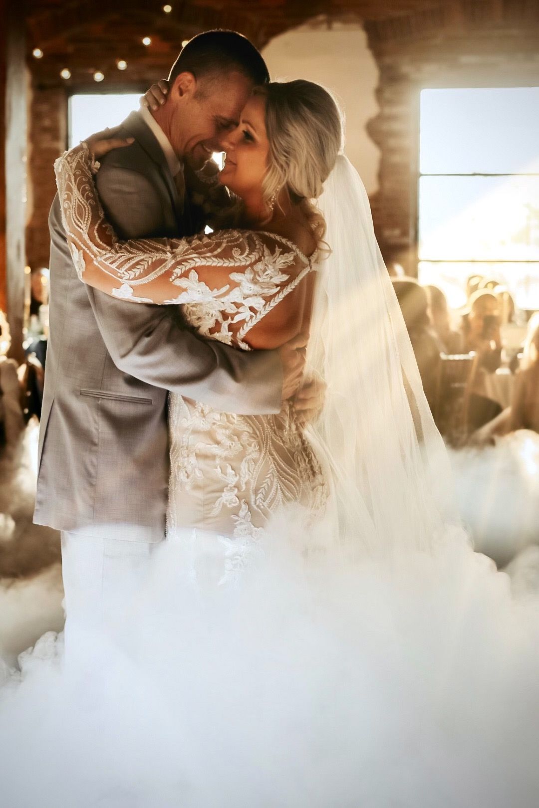 A bride and groom are dancing in front of a cloud of smoke.