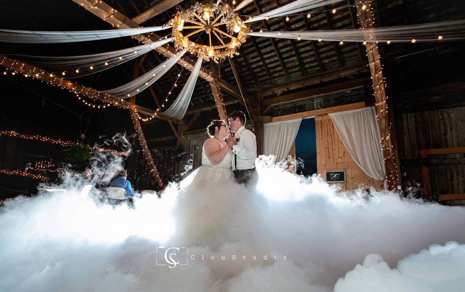 A bride and groom are dancing in a barn surrounded by smoke.