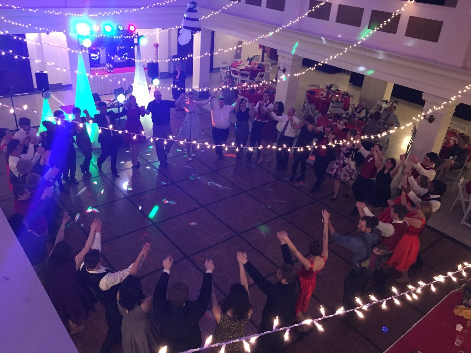 A group of people are dancing in a large room with lights hanging from the ceiling.