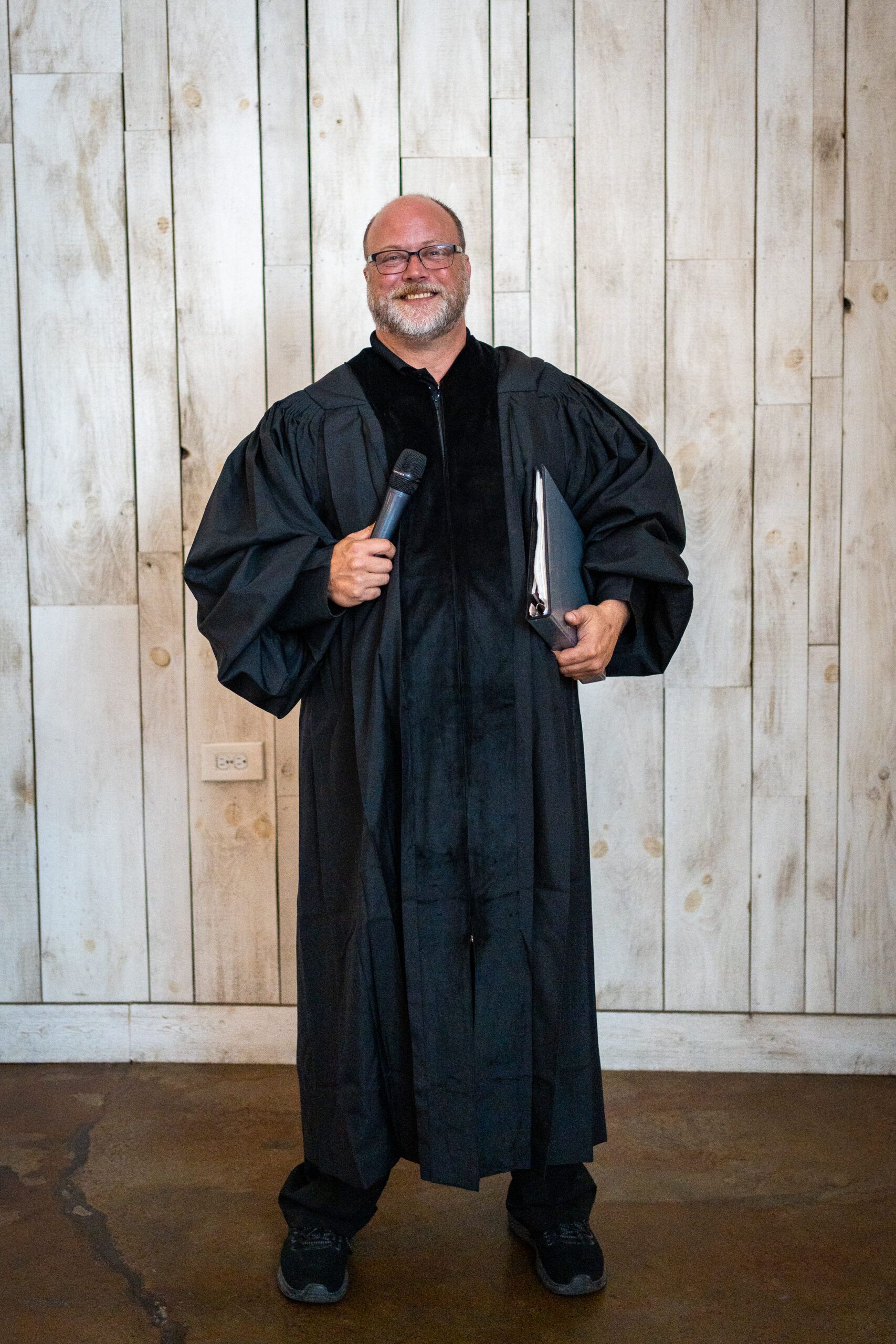 A man in a black robe is holding a microphone and a book.