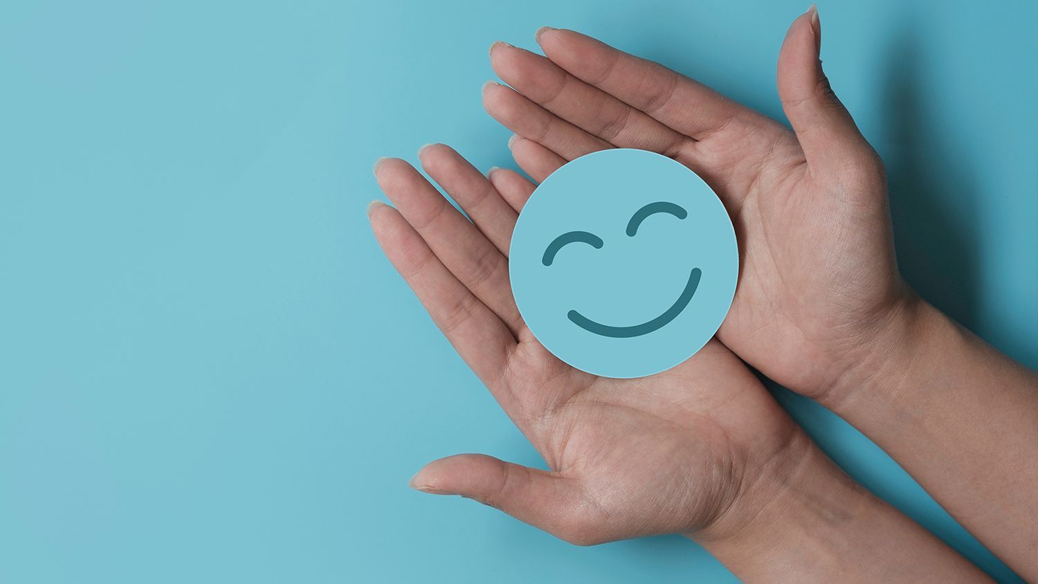 A person is holding a paper smiley face in their hands.