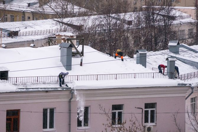 Snow-covered rooftop with several workers and chimneys in a residential neighborhood
