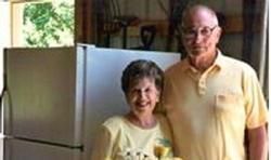 Couple smiling and posing by a refrigerator and utility area. Man in yellow shirt, woman in light top.