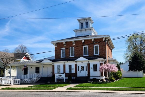 Brick building with white trim and a square tower on top, trees, blue sky.