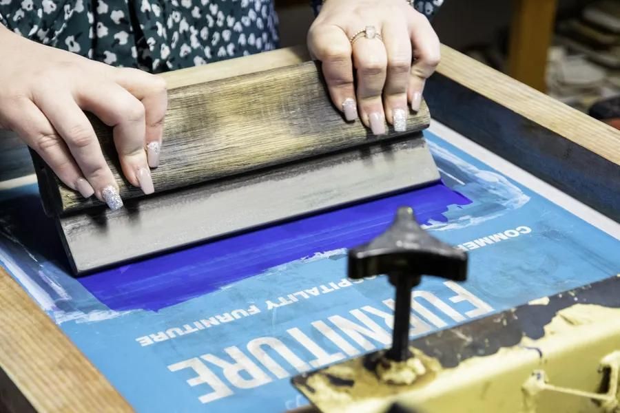 A Person Is Using A Screen Printing Machine To Print A Poster — Sportstar Screenprinting In Newtown, QLD