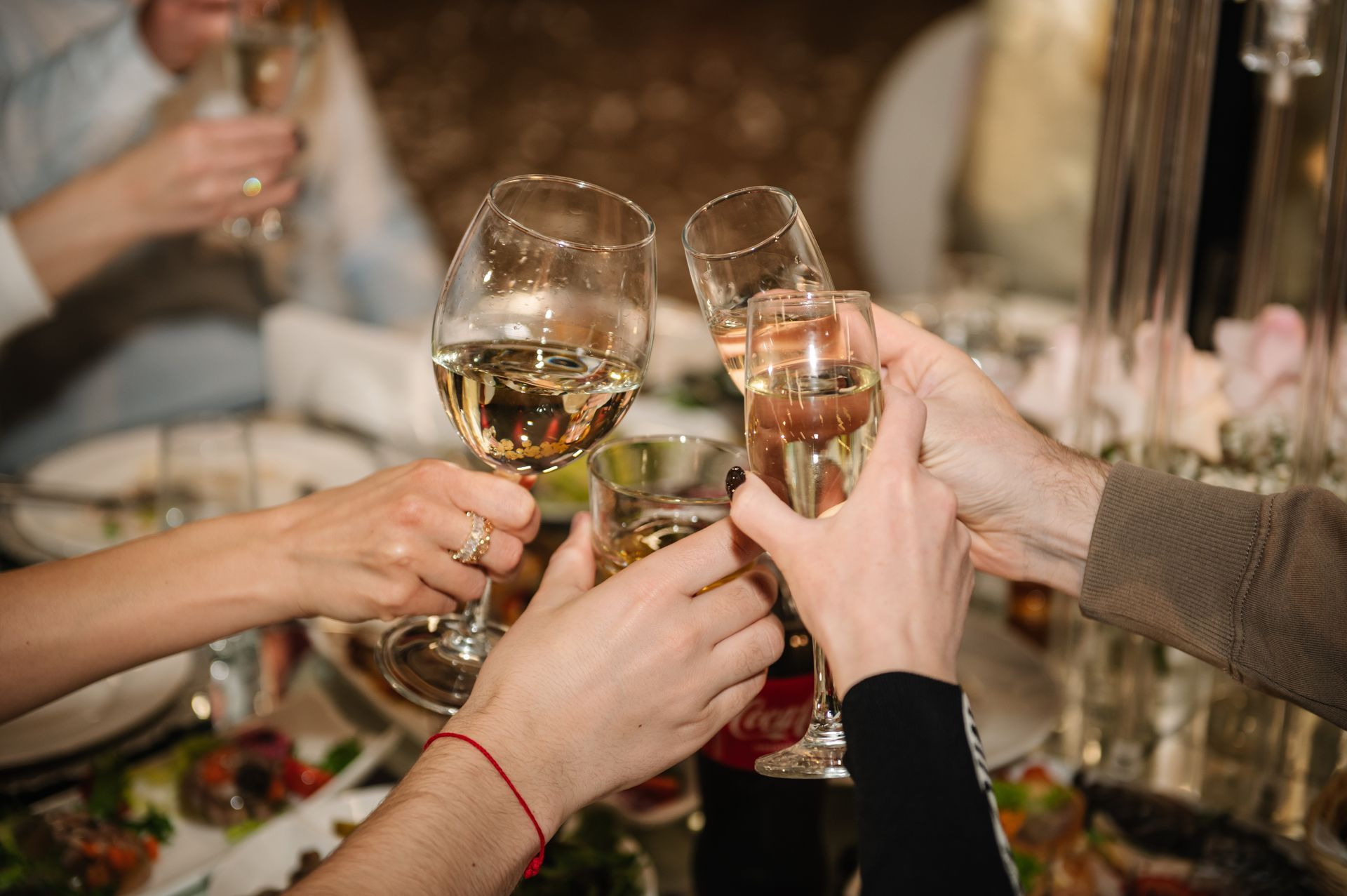 Hands raising champagne glasses at a festive dinner table with candles and flowers
