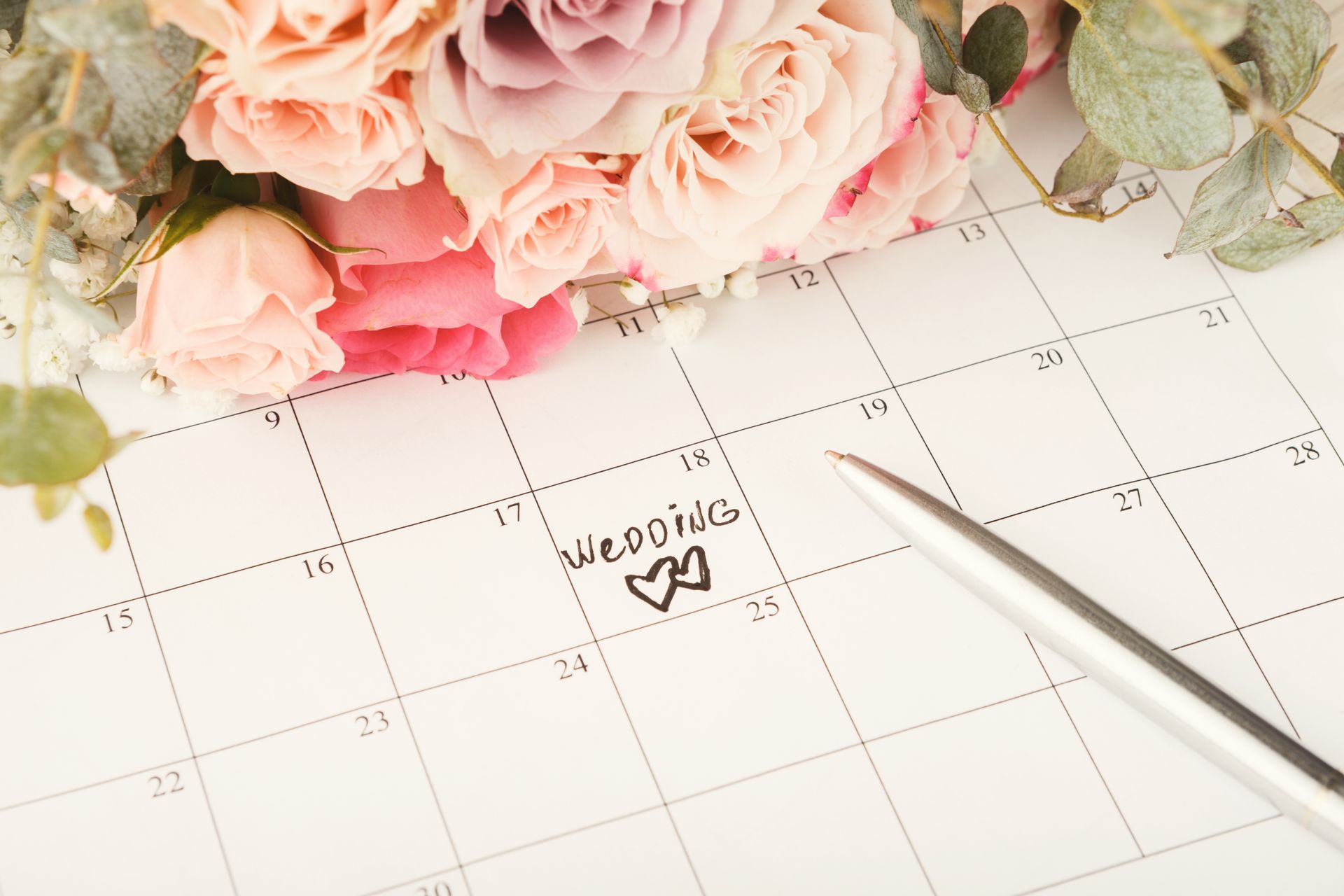 A calendar marked Wedding with a pen and a bouquet of pastel roses resting on top.