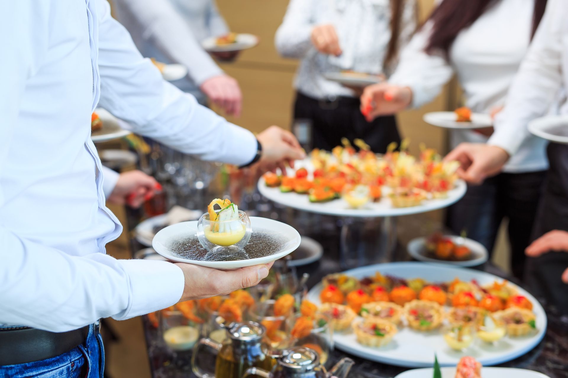 People serving appetizers at a catering buffet with trays of colorful finger foods