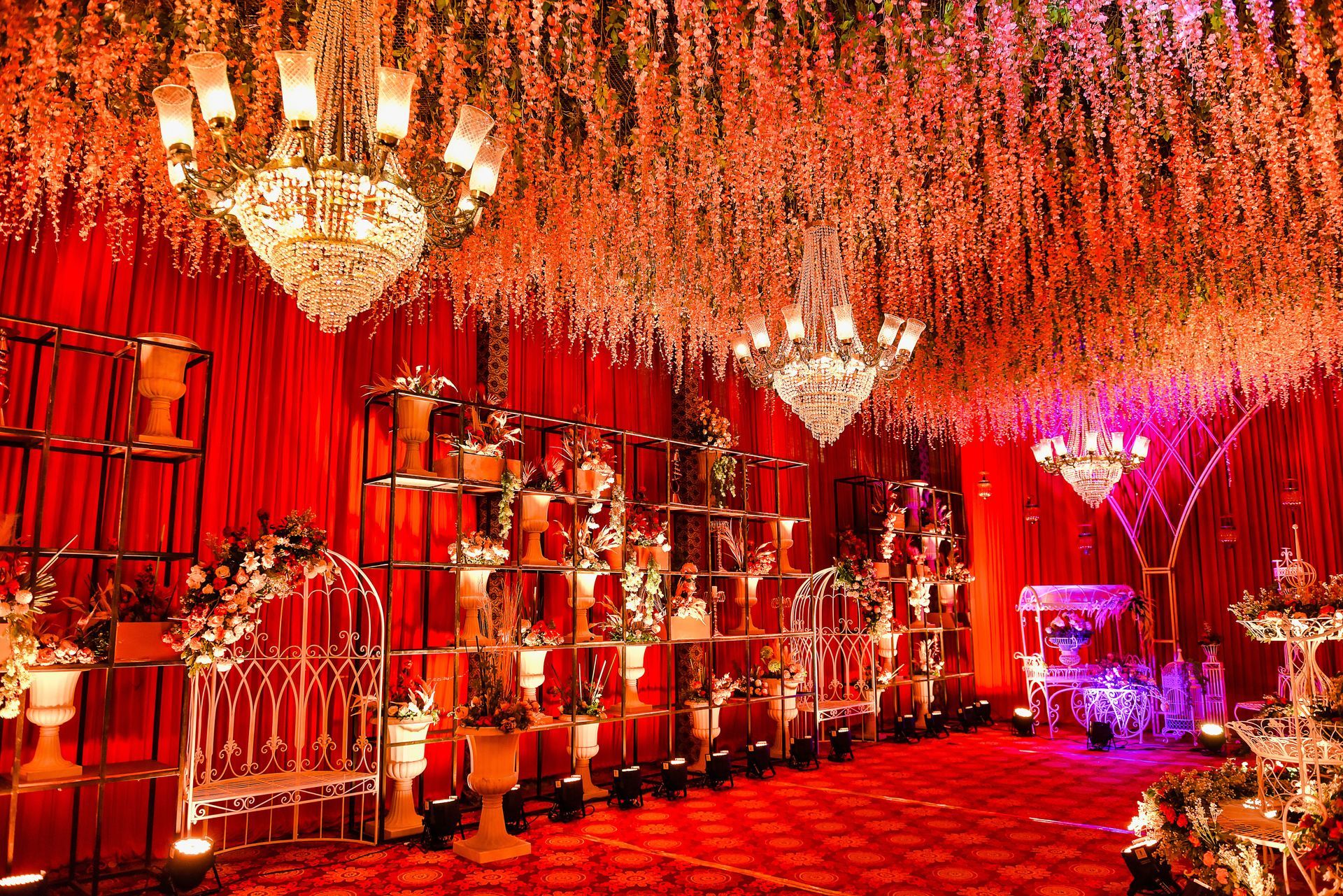 An elegant event space decorated with red curtains, crystal chandeliers, and a ceiling covered in cascading white flowers.