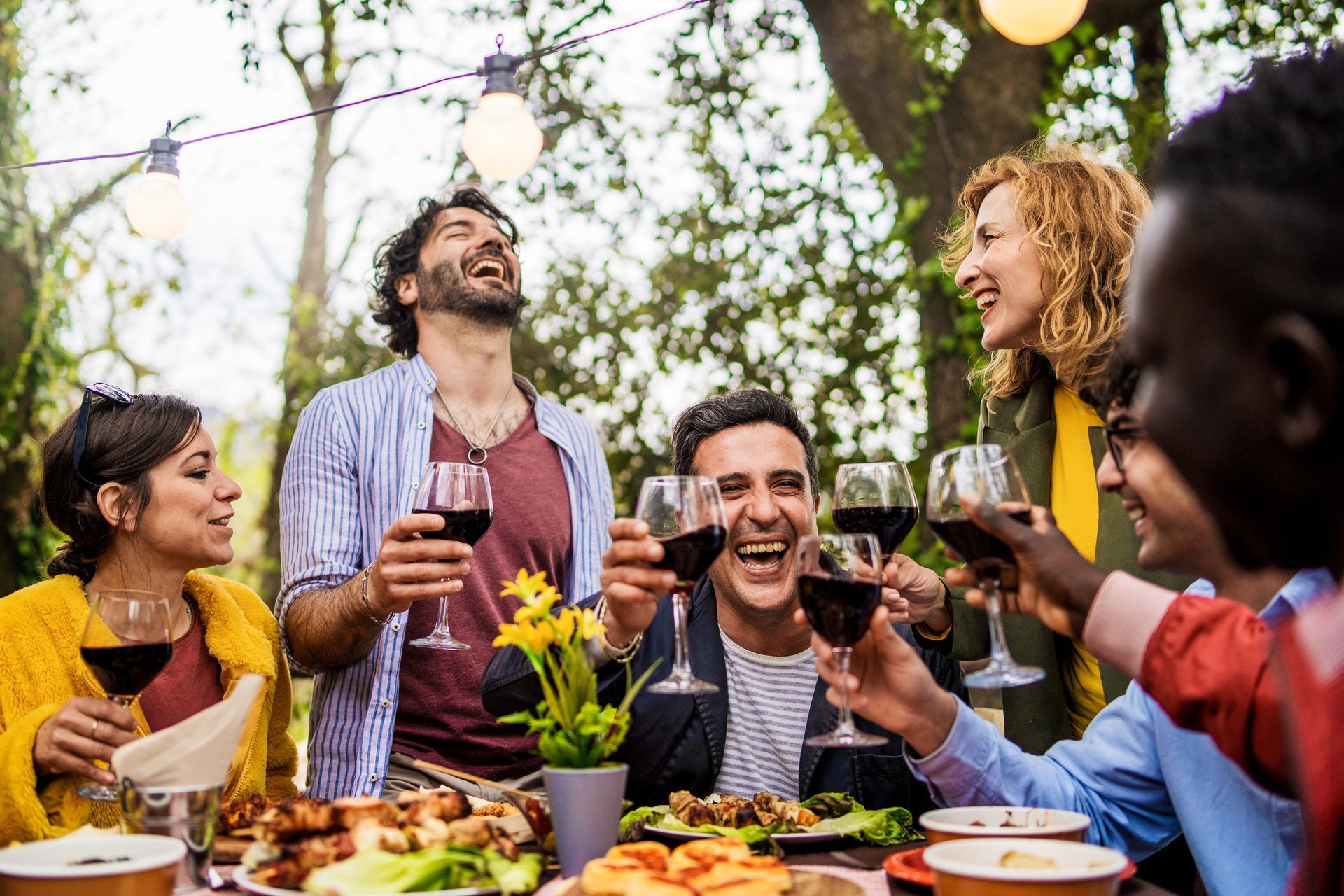 Friends toasting with wine at an outdoor dinner party under string lights