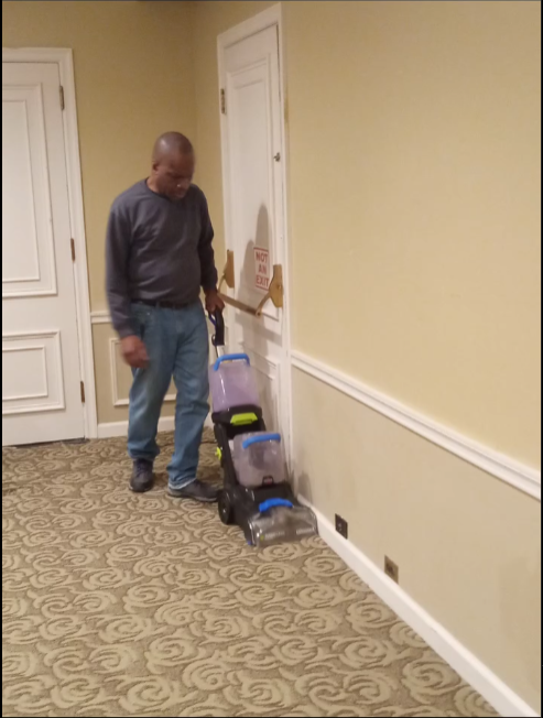 A man is cleaning a hallway with a vacuum cleaner