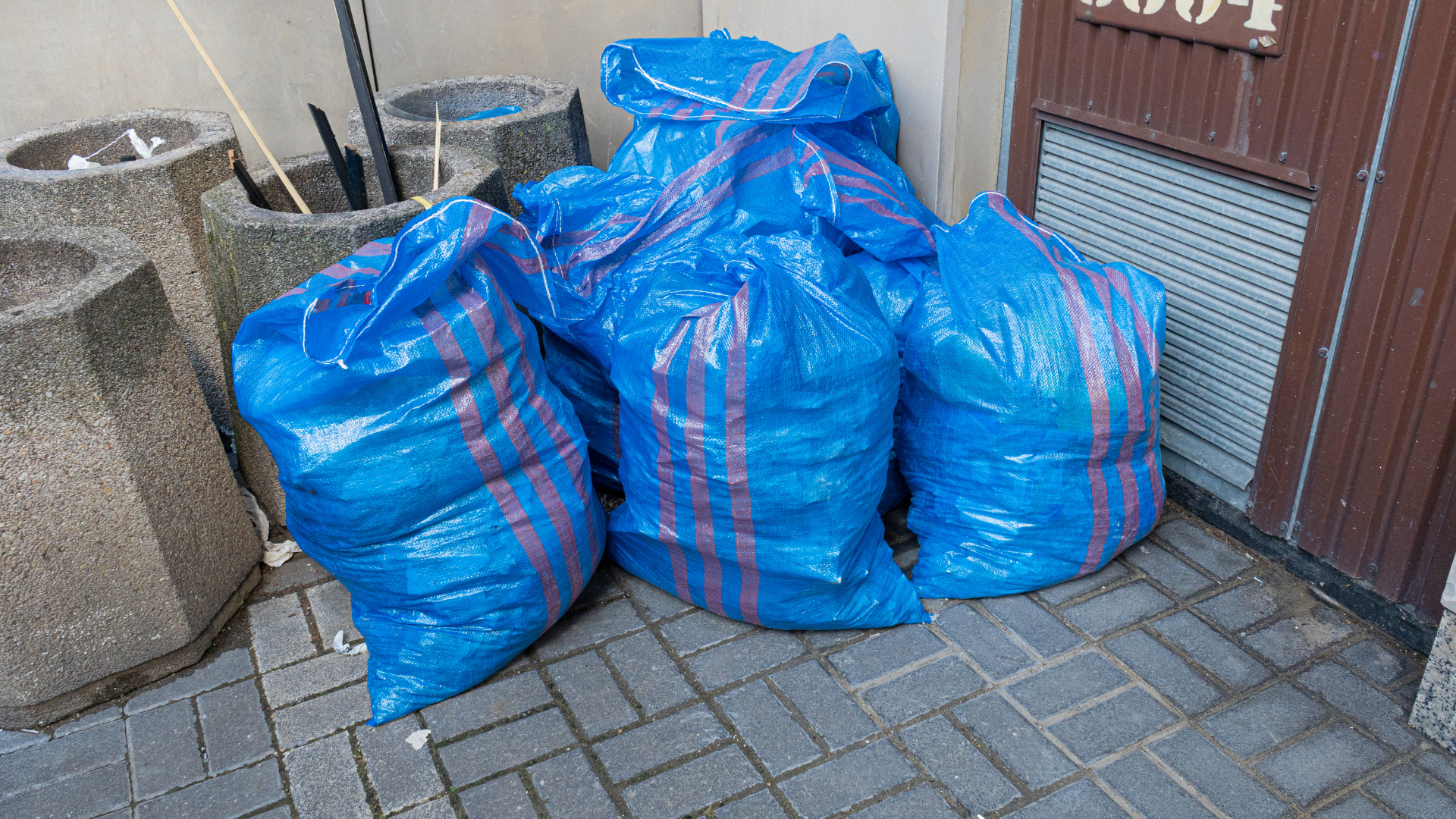 A bunch of blue bags are sitting on a brick sidewalk.