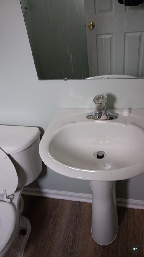 A bathroom with a toilet , sink and mirror.
