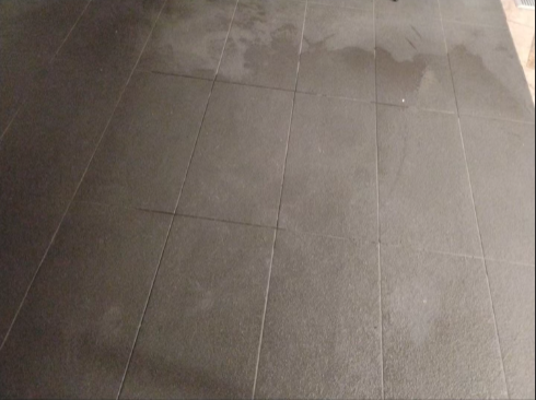 A black tiled floor with a few spots of water on it.