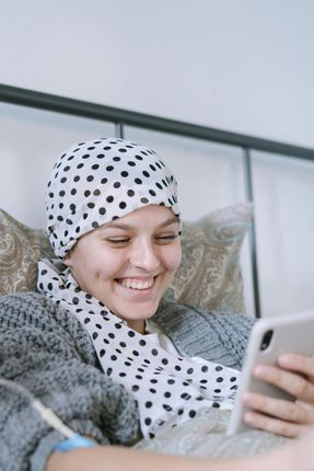 Person in bed wearing headscarf and smiling at a phone screen, appearing happy.