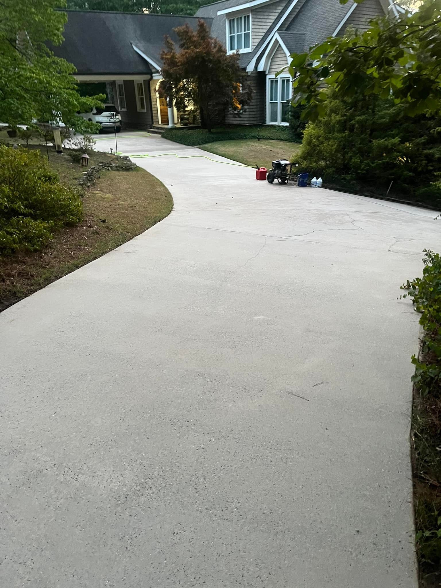 A concrete driveway leading to a large house surrounded by trees.